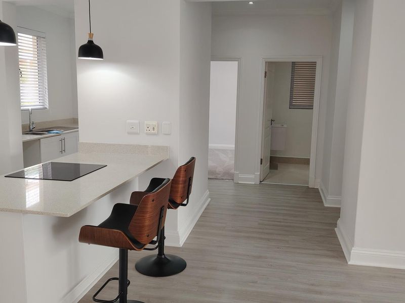 Modern open-plan kitchen area featuring stone countertops, integrated hob, and sleek cabinetry, flowing into a hallway leading to additional rooms.