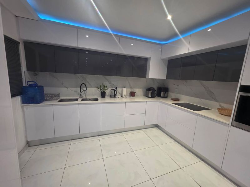 Modern kitchen featuring high-gloss cabinetry, marble-look splashback, integrated appliances, and ambient LED strip lighting.