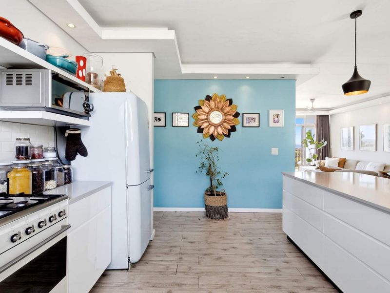 Modern open-plan kitchen and living area featuring a central island, gas hob, built-in oven, and sleek white cabinetry with contemporary finishes.
