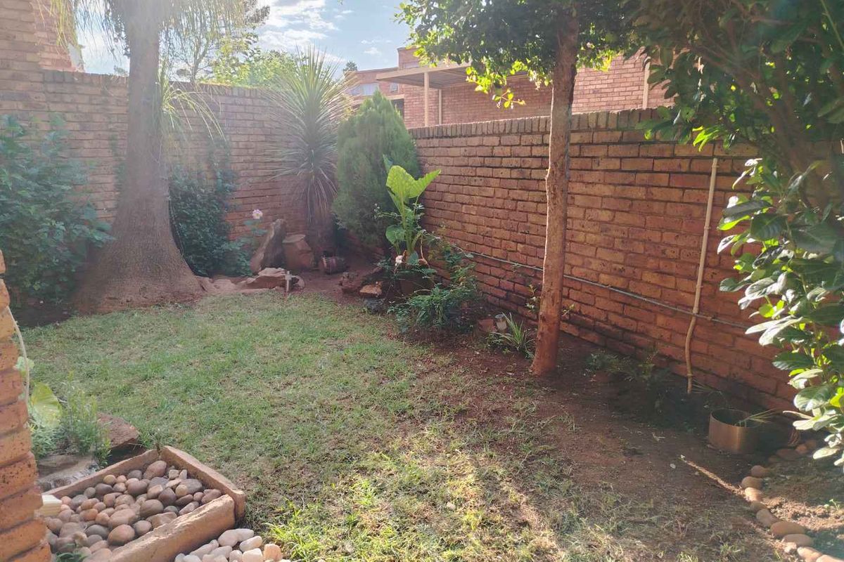 A private rear garden featuring established trees, a small lawn area, and perimeter brick boundary walls.