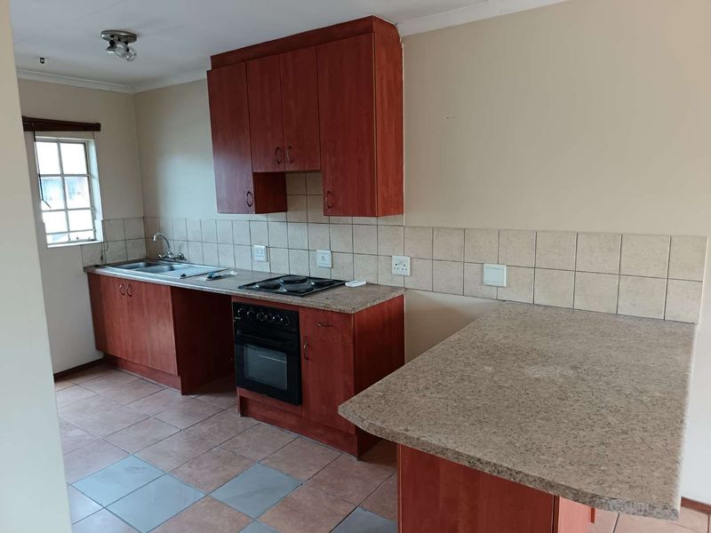 A functional kitchen featuring wood-tone cabinetry, laminate countertops, a built-in oven with hob, and tiled flooring, offering a clean and practical workspace.