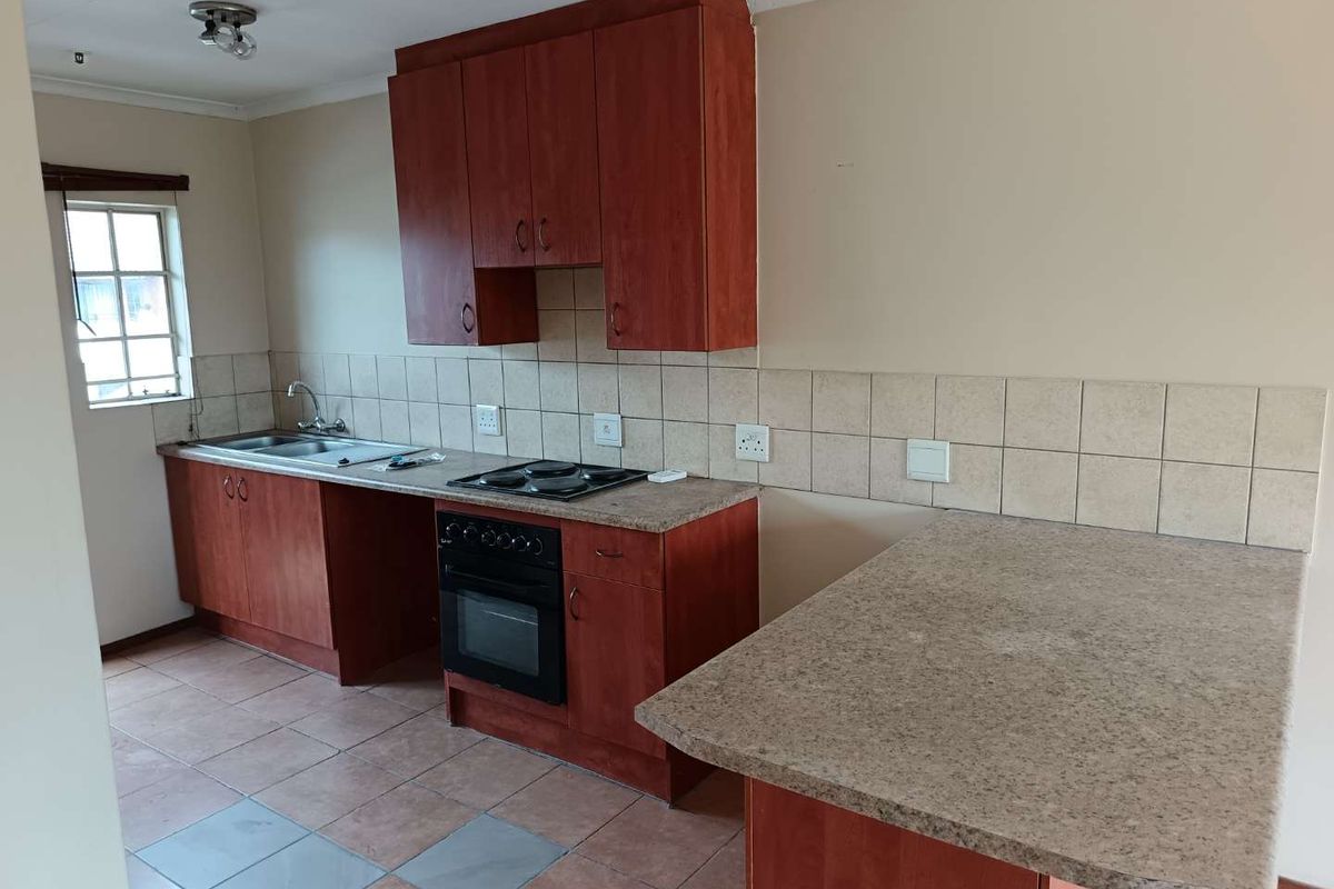 A functional kitchen featuring wood-tone cabinetry, laminate countertops, a built-in oven with hob, and tiled flooring, offering a clean and practical workspace.