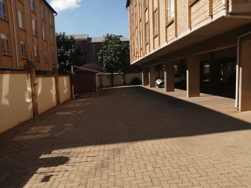 A paved exterior rear parking area featuring covered parking bays supported by concrete pillars and enclosed by a brick boundary wall.