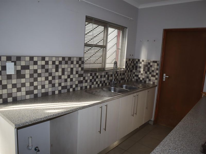 A functional kitchen featuring laminate countertops, a double bowl stainless steel sink with a gooseneck mixer, and a decorative tiled backsplash.