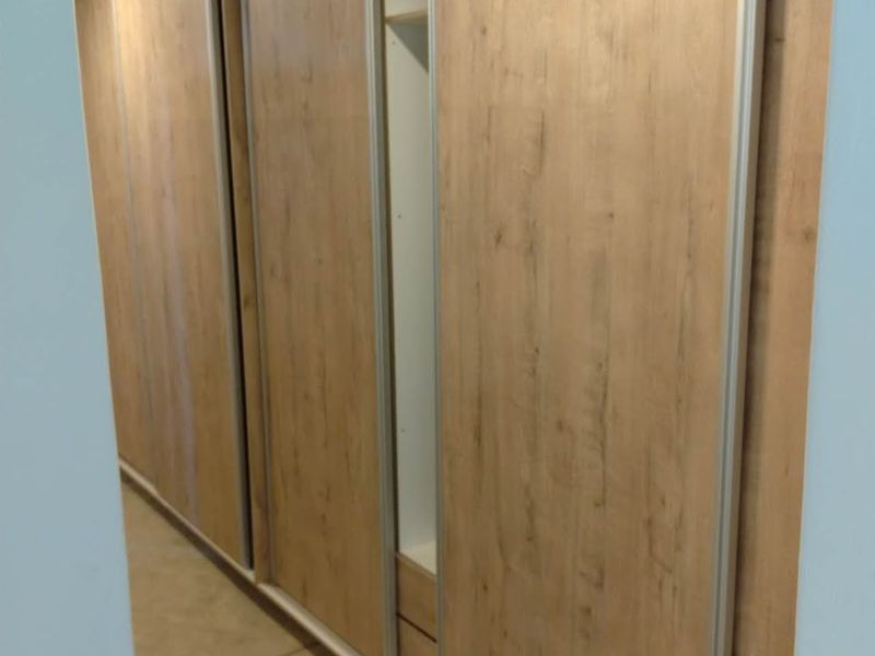 A clean bedroom interior featuring modern wood-finish built-in sliding door cupboards and neutral flooring.