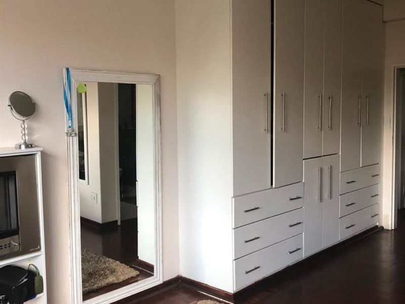 A bedroom featuring extensive white built-in cupboards with integrated drawers and dark wood flooring, complemented by crown molding.