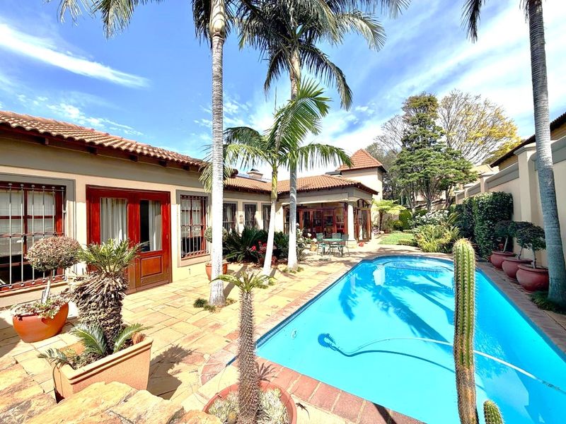 A well-maintained outdoor pool area featuring a tiled patio, mature palm trees, and direct access to the home through wooden double doors.