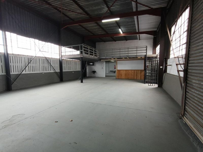 Spacious industrial warehouse unit featuring a mezzanine level, concrete flooring, exposed steel trusses, and a roller shutter door, suitable for various commercial operations.