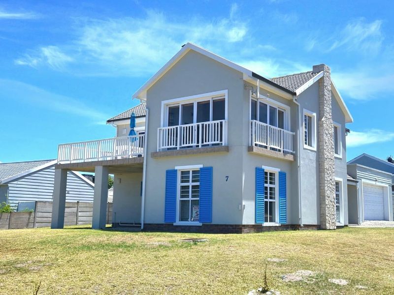 A well-maintained two-story house featuring a raised patio, balcony, stone-clad chimney, and blue shutters, set against a clear blue sky.