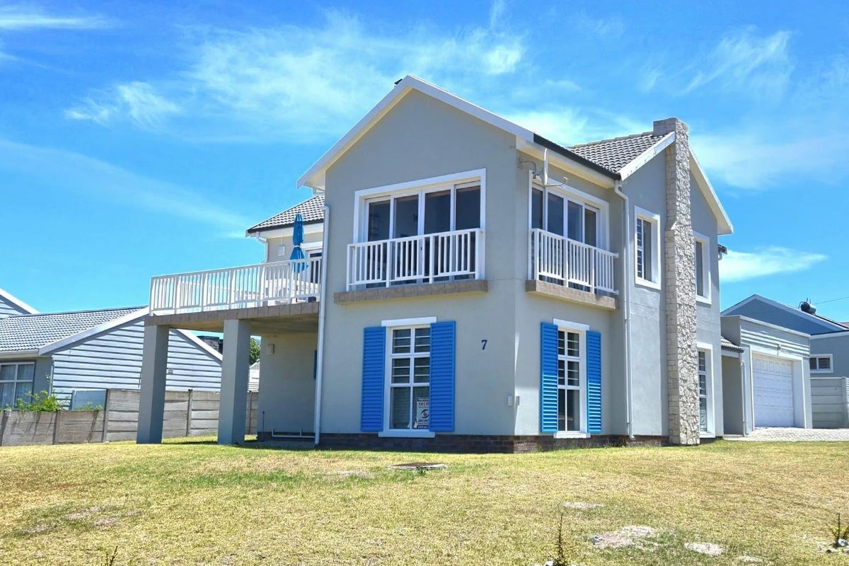 A well-maintained two-story house featuring a raised patio, balcony, stone-clad chimney, and blue shutters, set against a clear blue sky.