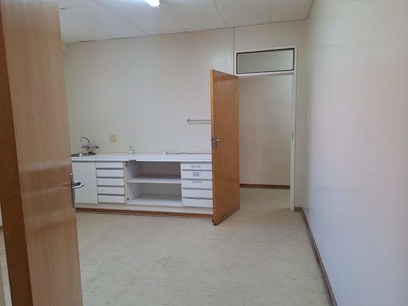 An empty office space featuring built-in cabinetry with an integrated sink, drop ceiling, and neutral finishes, suitable for a professional workspace.