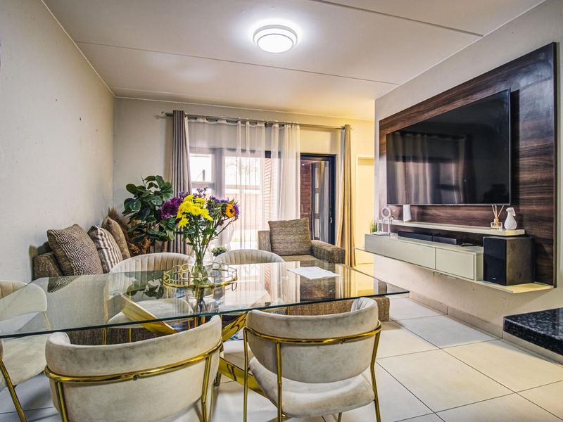 A well-maintained open-plan living and dining area featuring tiled floors, a modern wall-mounted media console, and a decorative wood-look feature wall.
