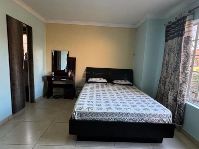 A bedroom featuring tiled flooring, a built-in cupboard, and a window with security bars, offering a functional and well-lit living space.