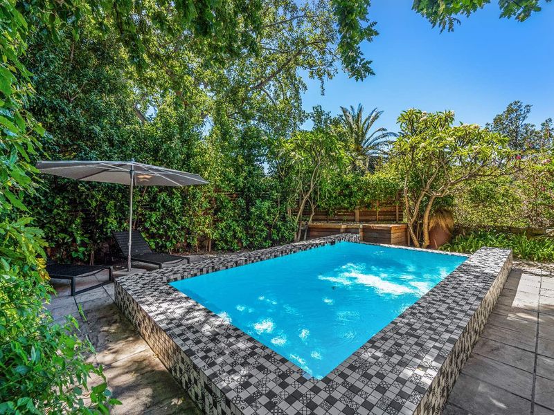 A private outdoor pool area featuring decorative tiled coping, surrounded by lush mature landscaping and paved patio space.
