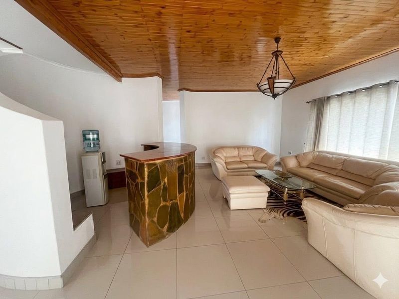Spacious living area featuring a unique built-in stone bar, warm timber ceiling, and neutral tiled flooring, offering a comfortable and functional layout.