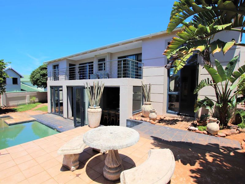 Rear view of the property featuring a tiled patio, swimming pool, and an upper-level balcony with stainless steel railings.