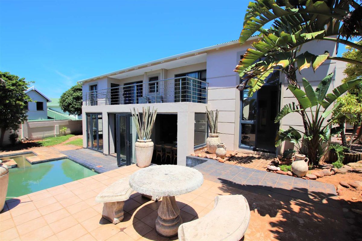 Rear view of the property featuring a tiled patio, swimming pool, and an upper-level balcony with stainless steel railings.