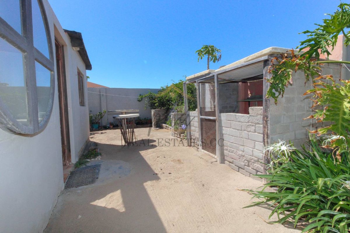 A rear exterior area featuring a sandy yard, perimeter boundary walls, and a basic outdoor utility structure.