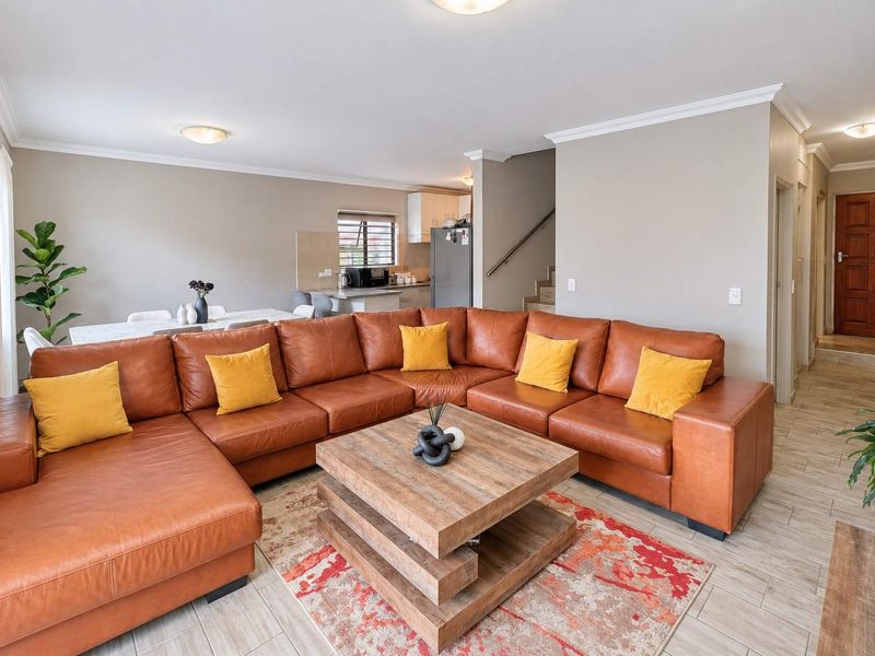 Spacious open-plan living and dining area featuring tiled floors, neutral walls, and a functional kitchen layout with direct access to the staircase.