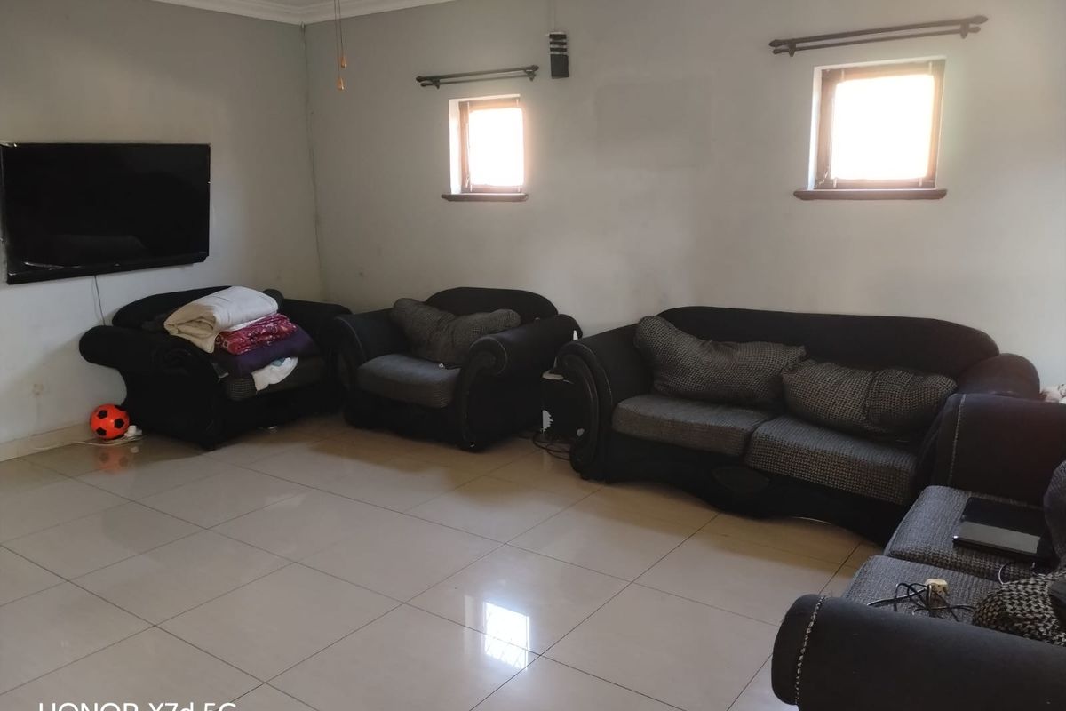 A spacious living room featuring tiled flooring, ceiling fan, and dual windows with curtain rods, offering a neutral base for interior updates.