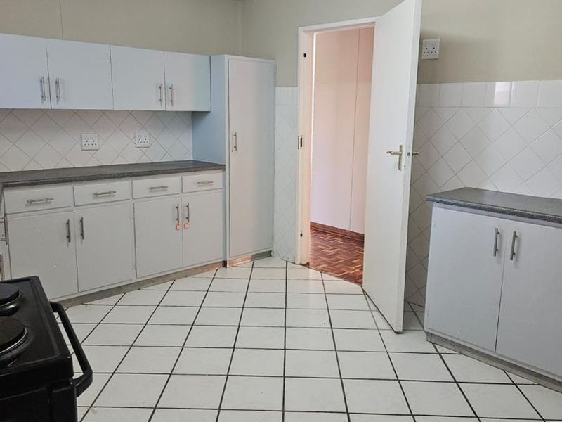 A functional kitchen featuring white built-in cabinetry, laminate countertops, tiled backsplash, and ceramic floor tiles, offering a clean and practical layout.