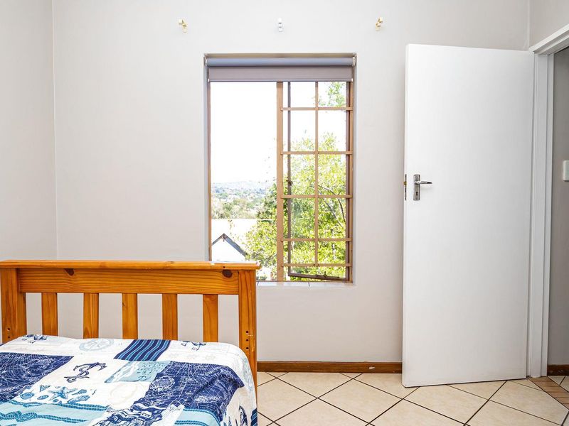 A bedroom featuring tiled flooring, a timber-framed window with a roller blind, and an internal door leading to an adjacent space.
