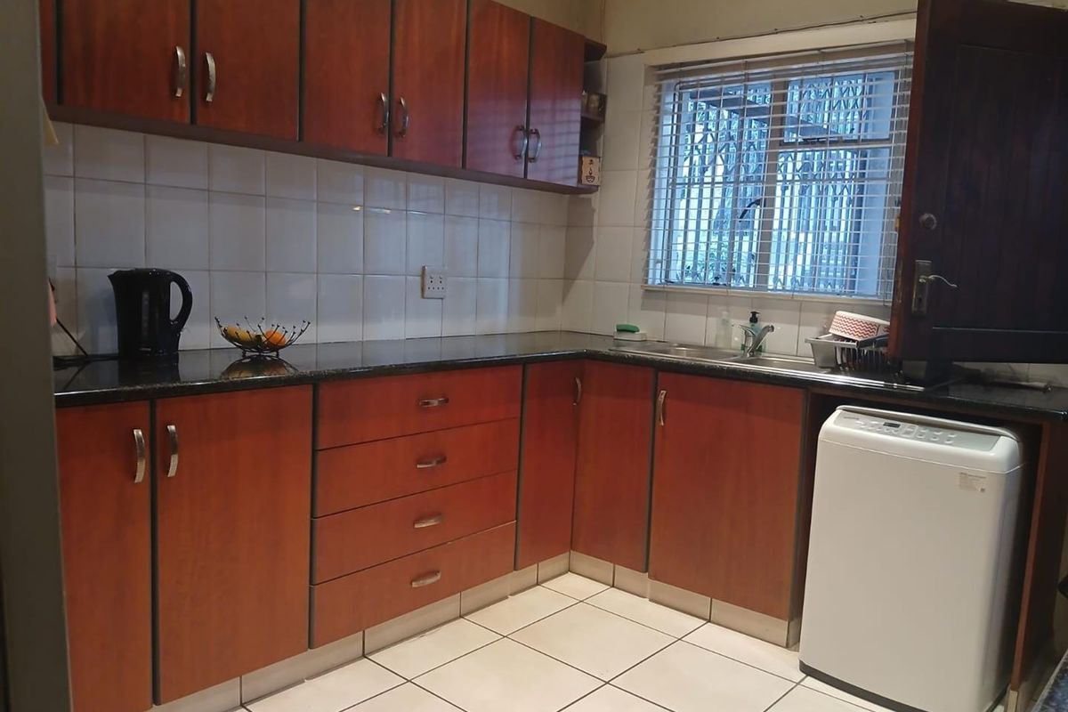 A functional kitchen featuring wood-look laminate cabinetry, granite countertops, tiled backsplash, and a stainless steel sink with security bars on the window.