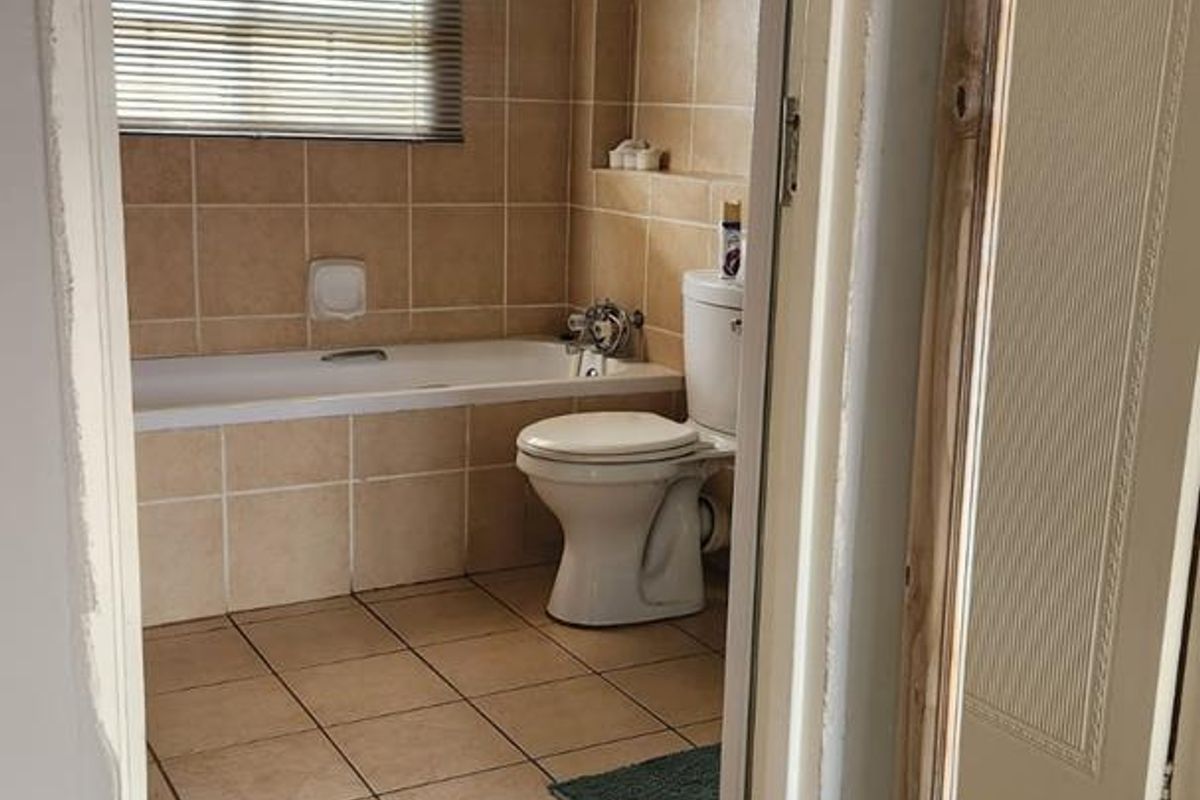 A functional bathroom featuring a built-in bathtub, ceramic floor and wall tiling, and a standard toilet, viewed from the adjacent hallway.
