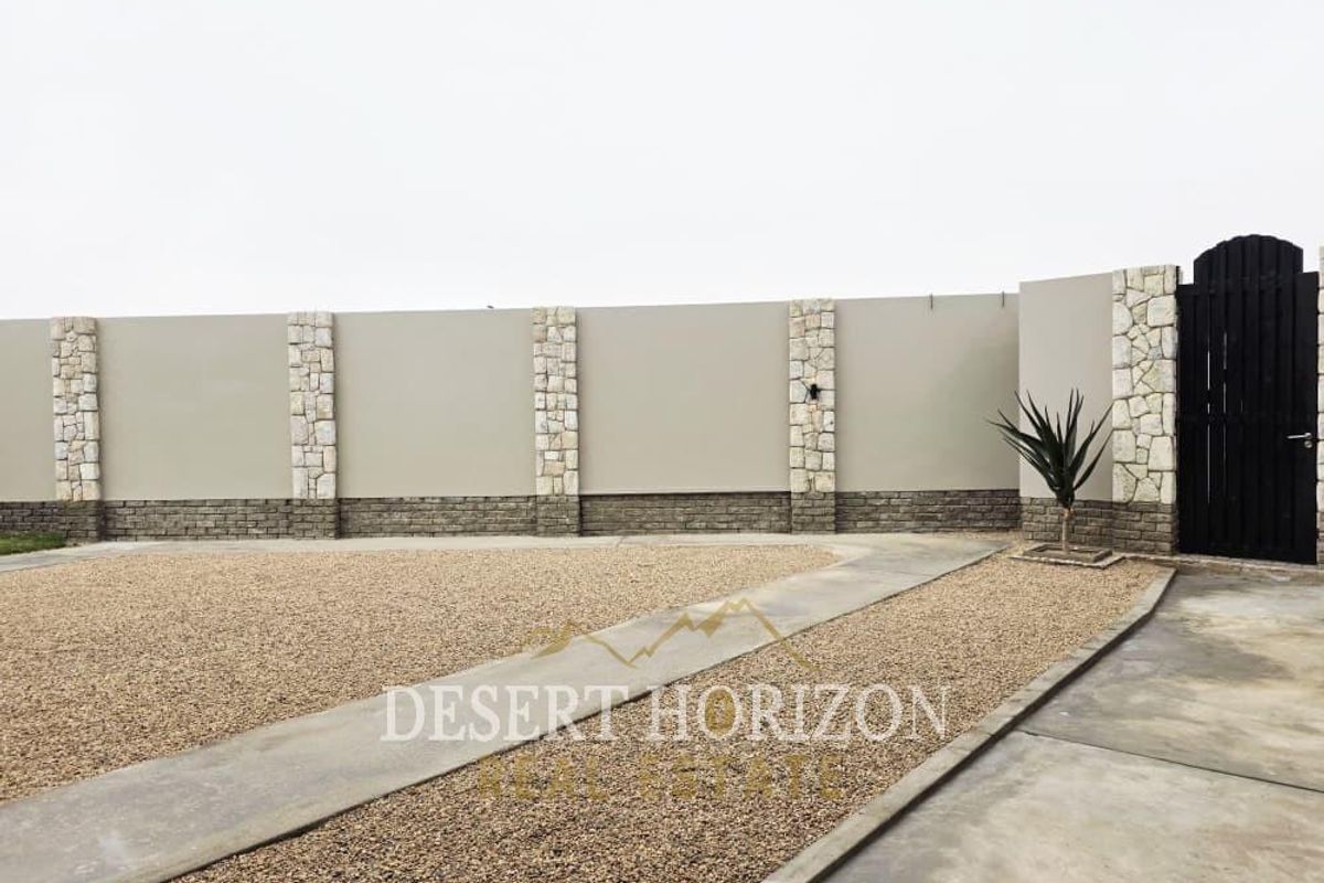A well-maintained exterior area featuring a high boundary wall with stone-clad pillars, a brick base, and a secure pedestrian gate.