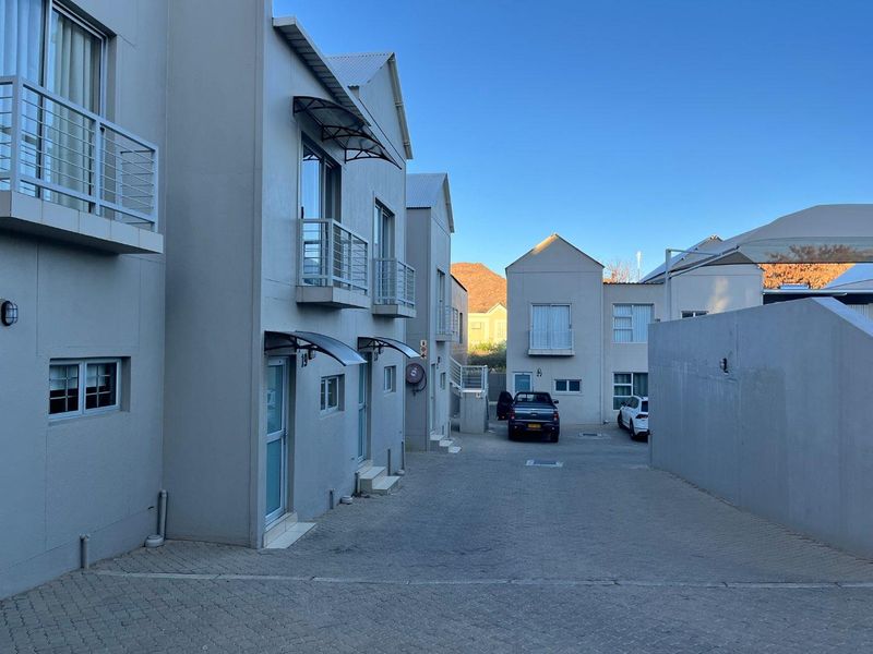 Exterior view of a modern apartment complex featuring paved driveway access, multiple balconies with metal railings, and clean architectural lines.