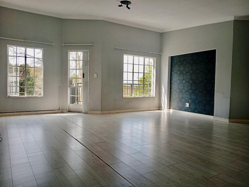 Spacious, light-filled living area featuring laminate flooring, an accent wall, and direct access to an outdoor balcony through a glass panel door.