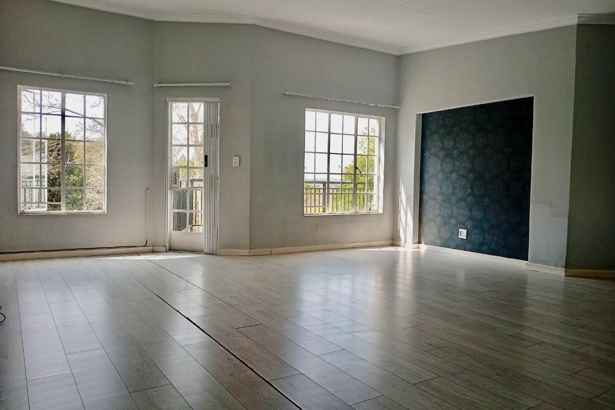Spacious, light-filled living area featuring laminate flooring, an accent wall, and direct access to an outdoor balcony through a glass panel door.