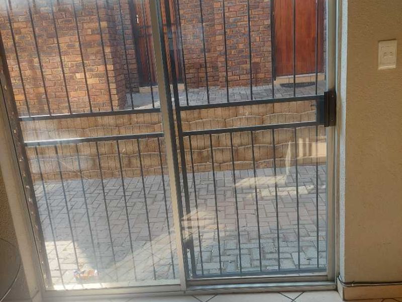Interior view of a living area featuring ceramic floor tiles and a sliding glass door with a security gate leading to an exterior brick patio.