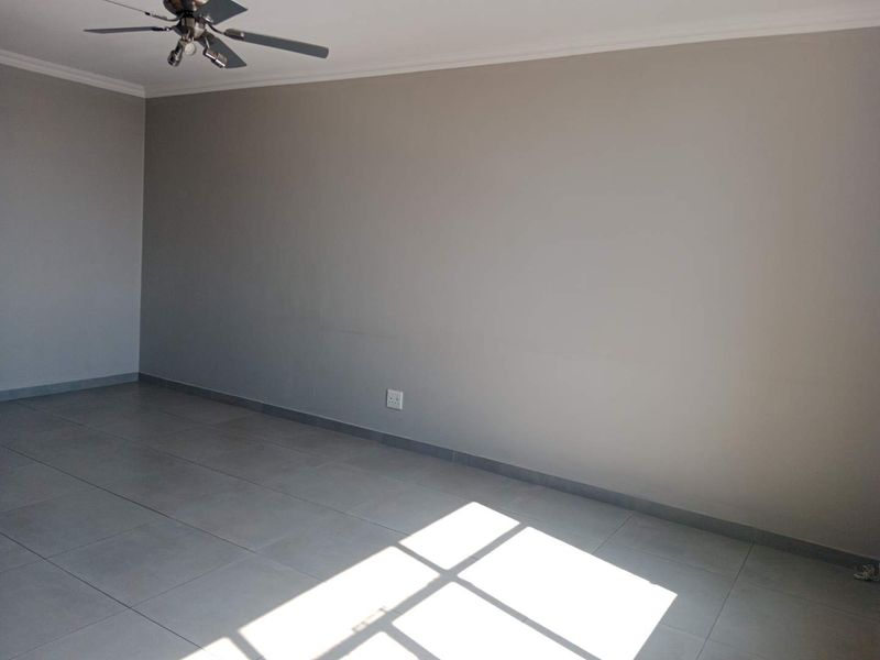A spacious, empty living area featuring neutral grey tiled flooring, coving, and a ceiling fan, offering a clean canvas for interior design.
