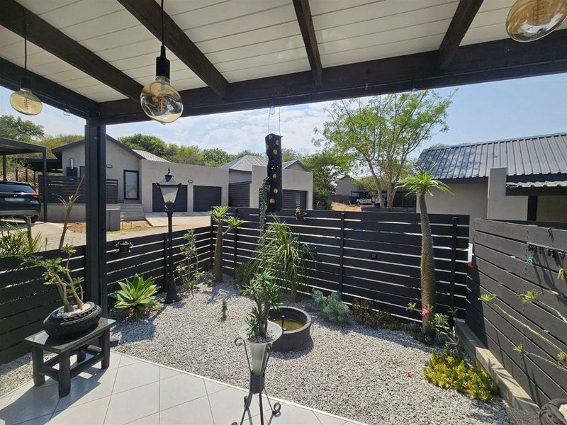 A well-maintained covered patio featuring a timber pergola, tiled flooring, and modern horizontal slat fencing, overlooking a landscaped garden area.