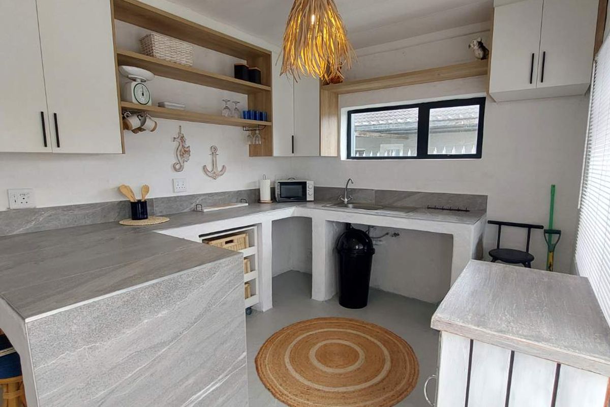 A compact, modern kitchen featuring white cabinetry, stone-look countertops, open shelving, and a functional sink area with a clean, minimalist aesthetic.