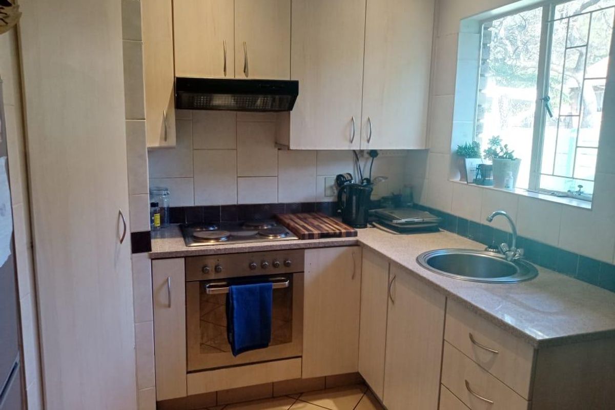 A functional kitchen featuring light-toned cabinetry, a built-in oven and hob, tiled backsplash, and a stainless steel sink with natural light.