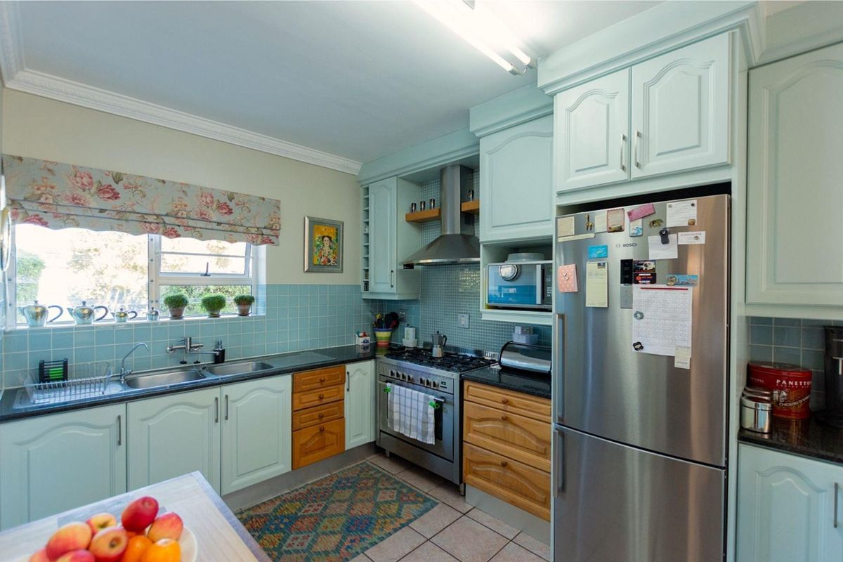 A functional kitchen featuring light-toned cabinetry, a stainless steel gas stove with extractor fan, double sink, and tiled backsplash.