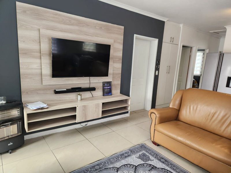 A well-maintained living room featuring a modern wood-look built-in media unit, neutral tiled flooring, and integrated storage cupboards.
