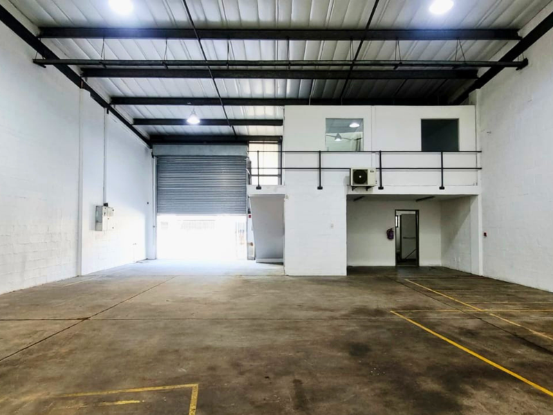 Spacious industrial warehouse unit featuring high ceilings with exposed steel trusses, a mezzanine level, concrete flooring, and a large roller shutter door.