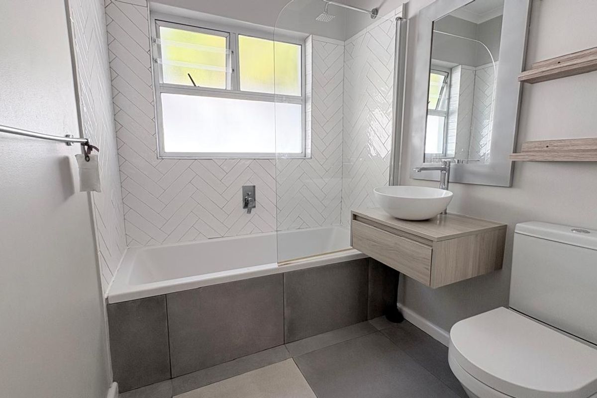 Modern bathroom featuring a white bathtub with a glass screen, herringbone wall tiling, a floating vanity with a vessel sink, and a toilet.