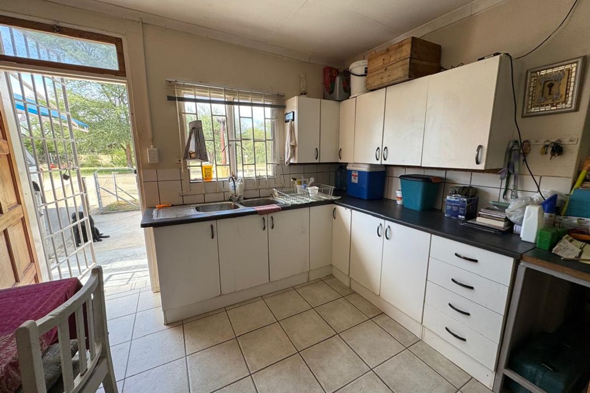 A functional kitchen area featuring white cabinetry, laminate countertops, a double sink, and tiled flooring with direct access to the exterior.