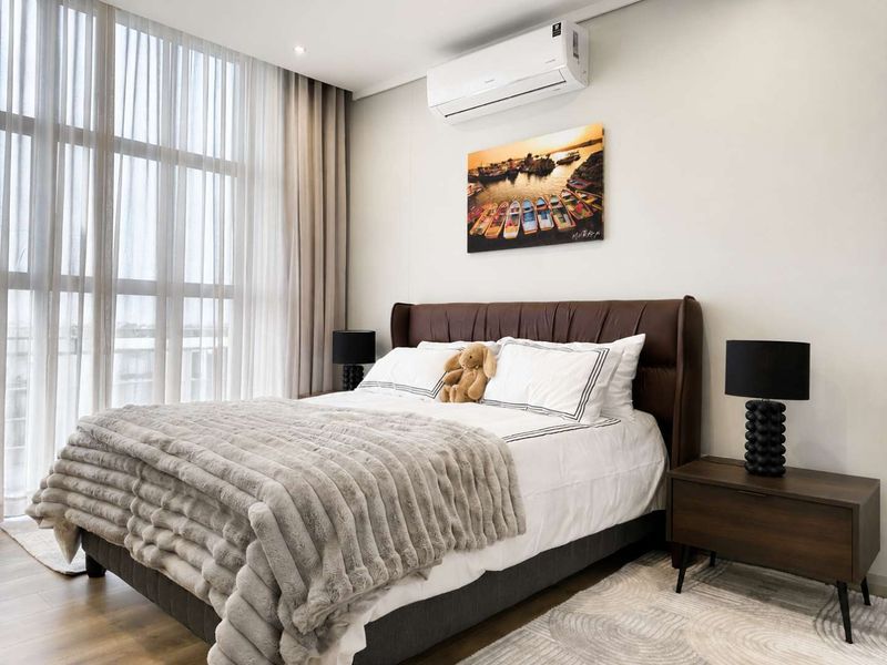A well-maintained bedroom featuring floor-to-ceiling windows, modern laminate flooring, and a wall-mounted air conditioning unit.