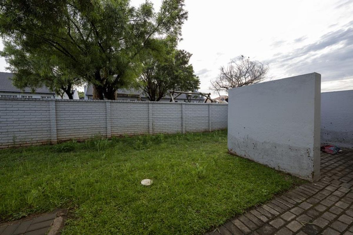 A private rear garden area featuring a paved section, lawn, and a perimeter brick wall with a standalone masonry privacy screen.