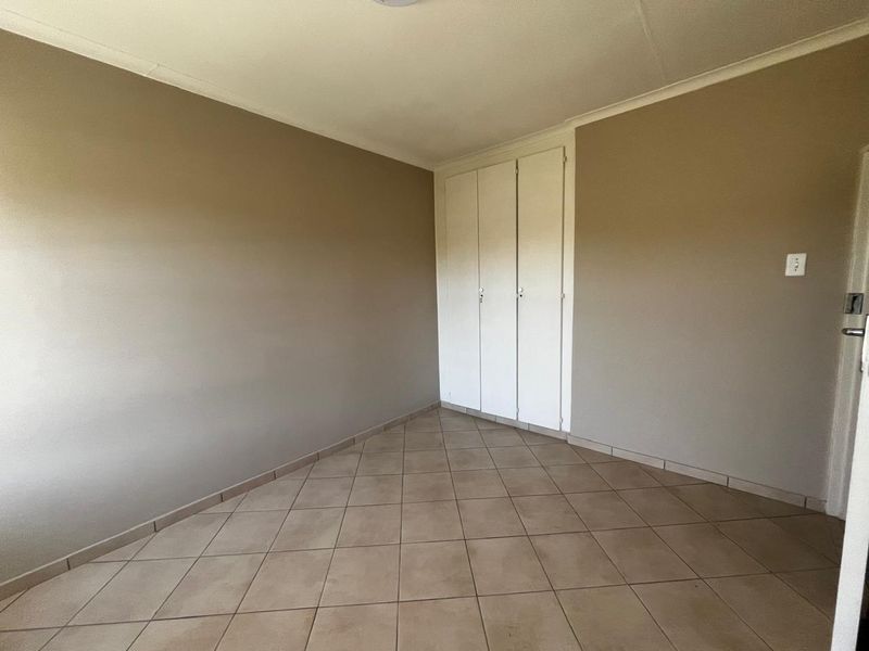 A clean, empty bedroom featuring neutral wall paint, tiled flooring, and built-in storage cupboards.