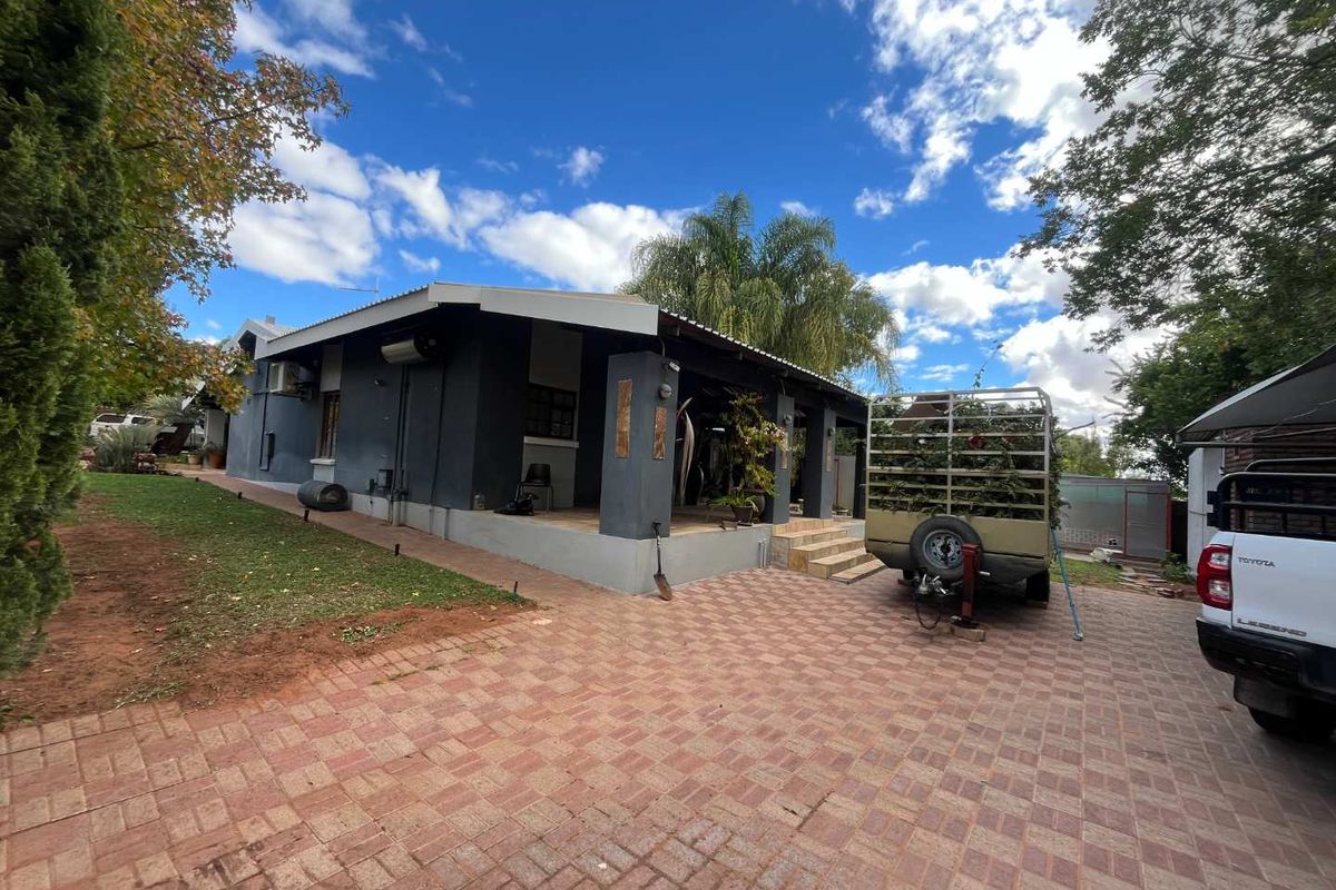 A view of the rear exterior of the house featuring a covered patio area, paved driveway, and surrounding garden space.