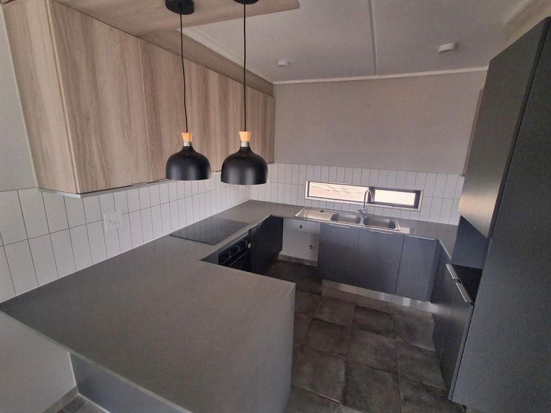 Modern kitchen featuring sleek grey cabinetry, stone countertops, integrated electric hob and oven, tiled backsplash, and contemporary pendant lighting.