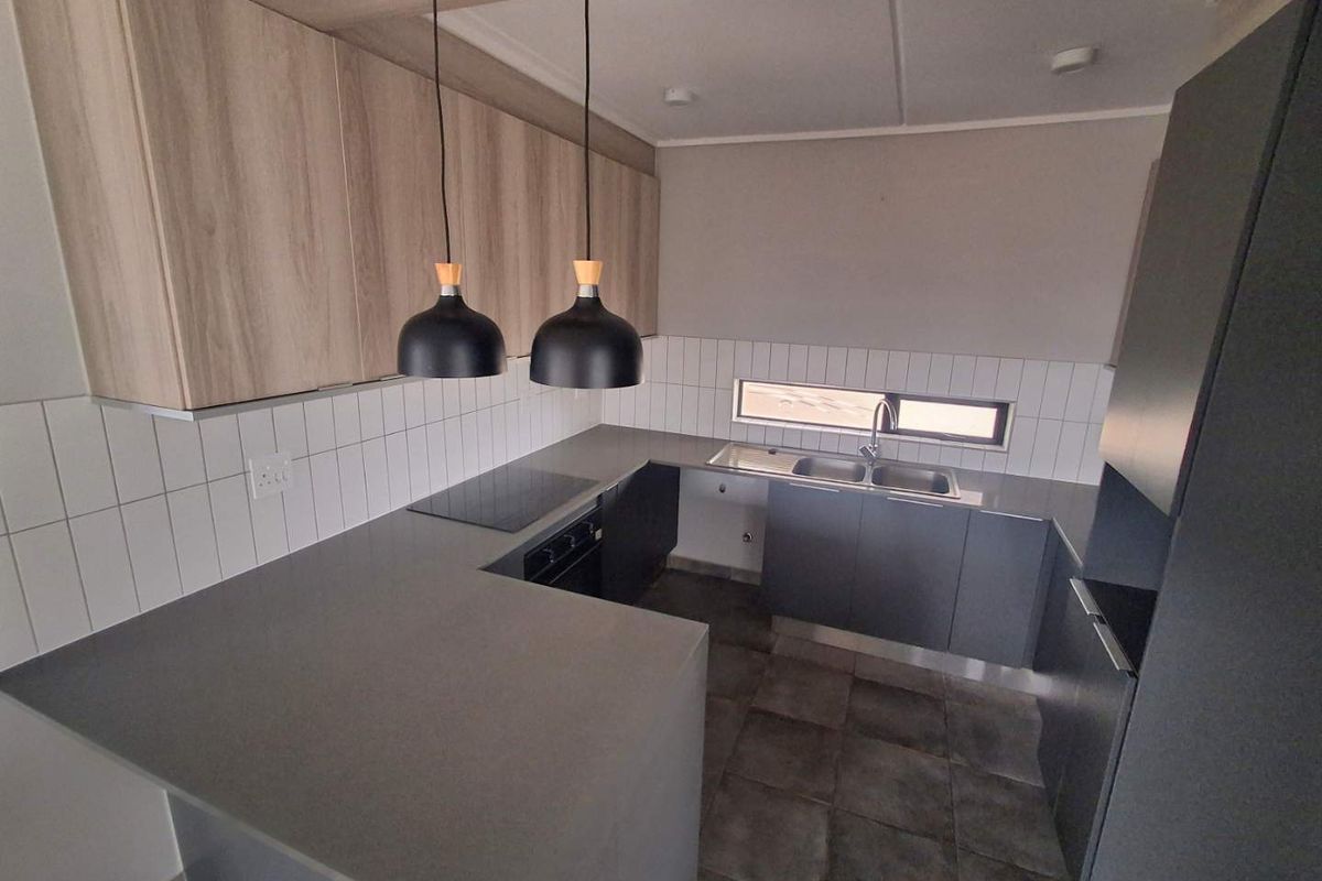 Modern kitchen featuring sleek grey cabinetry, stone countertops, integrated electric hob and oven, tiled backsplash, and contemporary pendant lighting.