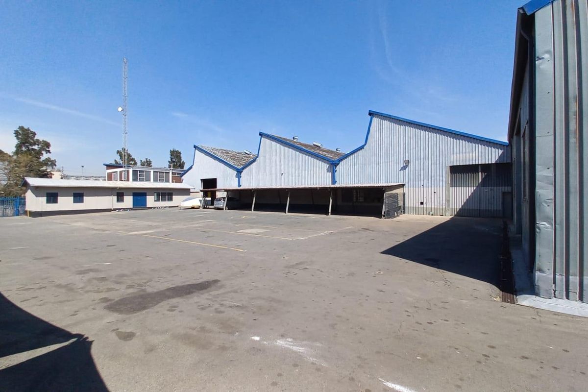 Rear industrial yard featuring a large asphalt area, covered loading bay, and sawtooth roof warehouse structure with metal cladding.