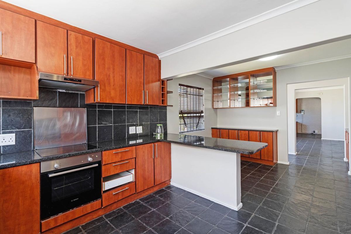 A functional kitchen featuring warm-toned wooden cabinetry, granite countertops, a built-in oven, and dark stone tile flooring with an integrated breakfast bar.